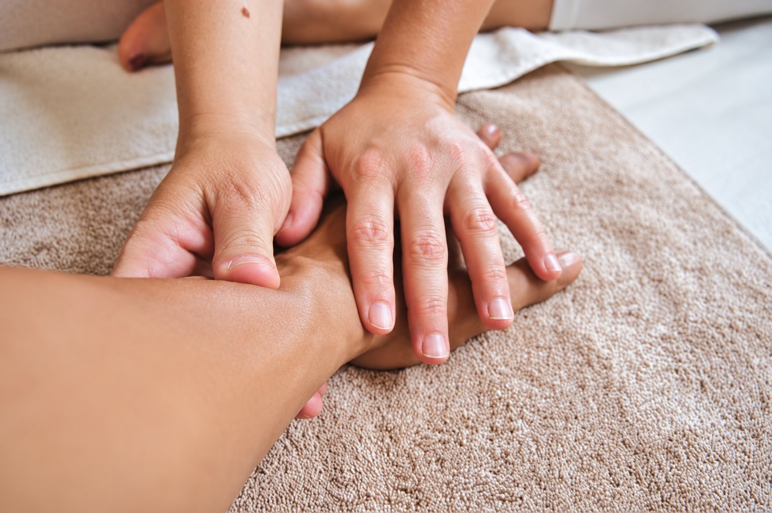 Gros plan sur les mains d'un praticien qui masse un bras posé sur une serviette éponge beige.